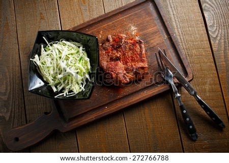 A delicious steak with red chili pepper, black plate of salad with fresh cabbage and rye toast croutons on wooden brown background