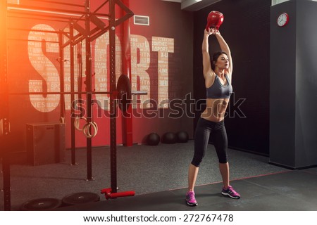 Strong and muscular young woman, brunette, holds up a red kettlebell in the gym