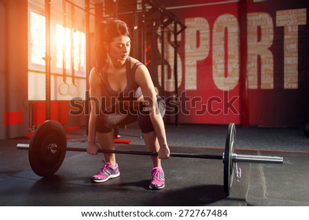 Strong and muscular young woman lifting a weight in the gym. The gym on the red wall is written SPORT