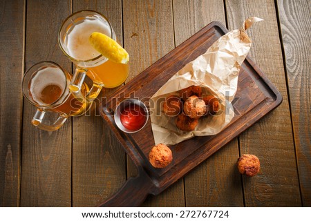 Cheese balls with spicy sauce in paper envelope on a dark wooden board and two glasses of beer with lemon, view from the top