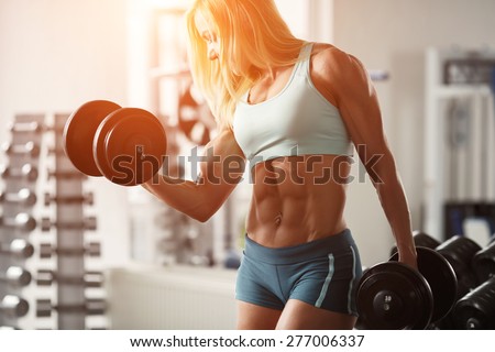 Strong woman bodybuilder with white hair and tanned body pumps up the muscles lifting dumbbells in the gym. Horizontal frame with space for text