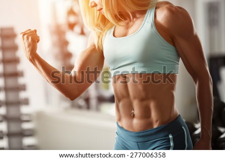 Brutal blond with a muscular, tanned body, straining biceps and abdominal muscles against the window in the gym, part of the body, horizontally frame