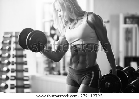 Black and white photo of a strong woman. Strong woman bodybuilder with white hair and tanned body pumps up the muscles lifting dumbbells in the gym. Horizontal frame with space for text