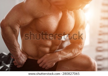 Brutal man bodybuilder shows muscles of the chest, abdomen and arms. Strong man flexing his muscles. Part of the body close-up
