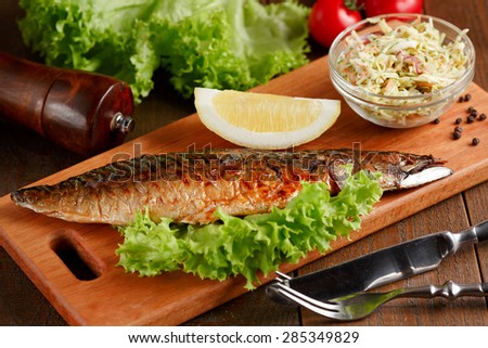 Close-up of fried mackerel with slice of lemon and lettuce on wooden cutting board
