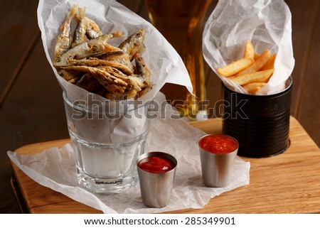 Close-up of beer snacks, sprat and french fries with gravy and glass of beer on wooden table