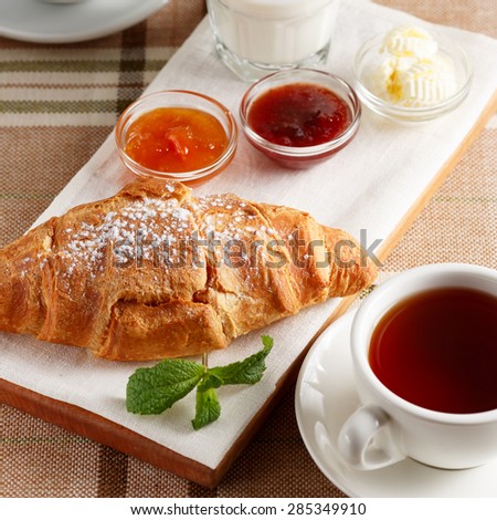 Close-up of croissant with jam, butter, cup of tea and yogurt
