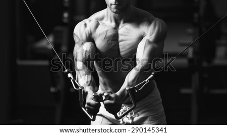 Young strong man black and white portrait. Muscular bodybuilder doing exercise on the chest in the crossover in the gym