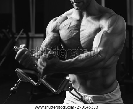 Young strong man black and white portrait. Strong muscular bodybuilder doing exercise on the chest in the crossover in the gym