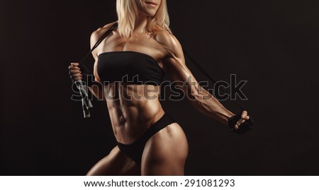 Confident young fitness female looking away and posing with jumping rope in the studio on a black background. Front view of woman bodybuilder with jumping rope. Space for text on the right side