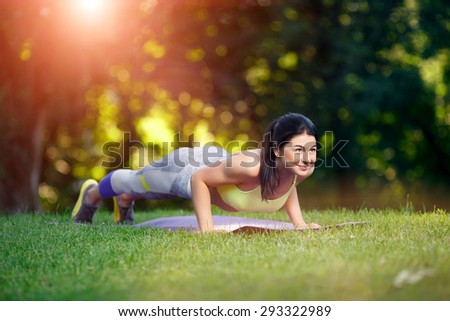 Young smiling woman doing fitness exercises in the park on the green grass. Fitness training in the sunlight.