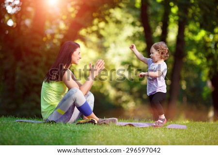 Young athletic girl with child doing exercises outdoors.