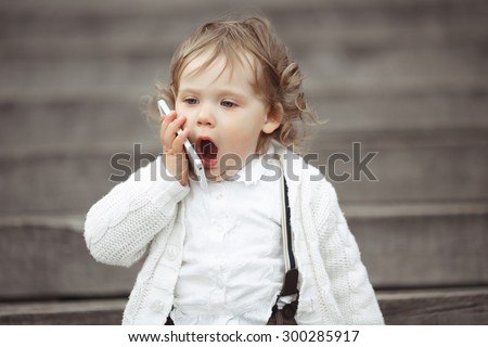 Cute little girl in white knitted sweater talking on mobile phone outdoors