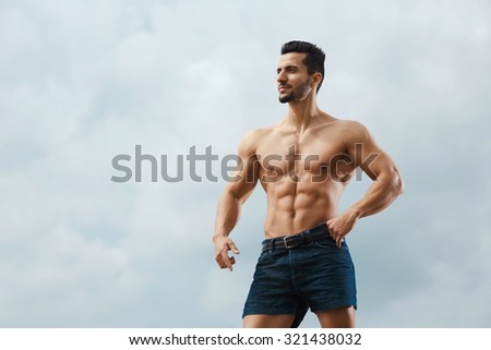 Muscular male torso on a background sky. Athletic and muscular man with naked torso posing on the sky background, looking away