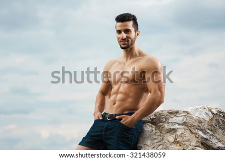 Muscular male torso on a background sky. Athletic and muscular man with naked torso stands on top of a mountain. Handsome young guy posing sporty appearance on the sky background