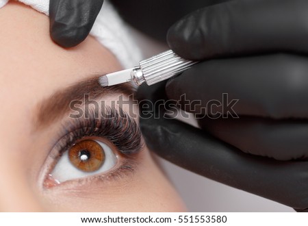 Permanent makeup eyebrows. Mikrobleyding eyebrows workflow in a beauty salon. Cosmetologist applying a special permanent makeup on a woman\'s eyebrows.