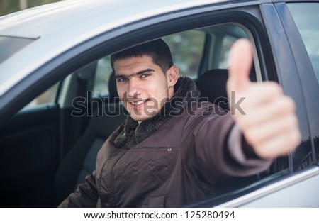 Young smiling driver thumb up in a car. Selective focus.