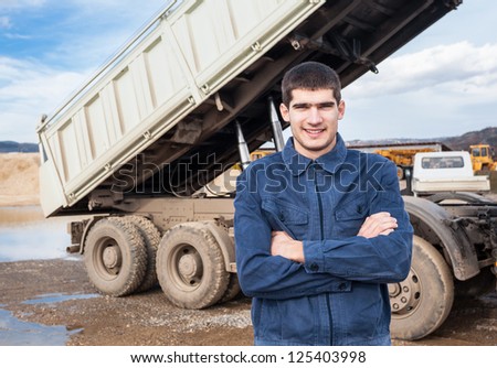 Young worker standing in front of big tip truck. Dump truck tipping load.