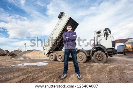 Young worker standing in front of big tip truck. Dump truck tipping load.