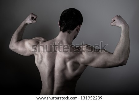 Muscular male back over dark background. Young bodybuilder posing in studio.