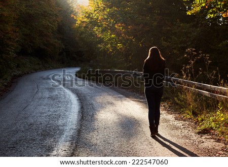 Woman walking on road in autumn afternoon. Beautiful autumn scene.
