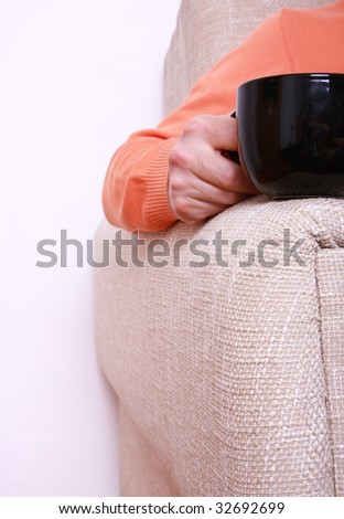 Man in orange blouse seating on the sofa and holding black cup.
