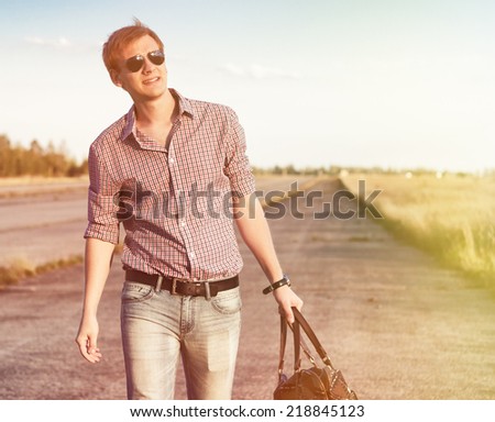 Young hipster man traveling with leather bag on sunny autumn field. Instagram filters, Copy-space. Freedom concept
