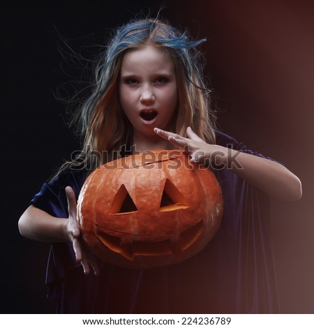 Image of a little girl posing with a pumpkin with witch make up on the dark grey background