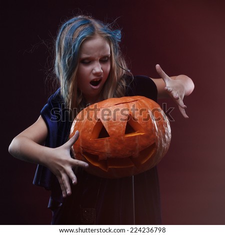 Image of a little girl posing with a pumpkin with witch make up on the dark grey background