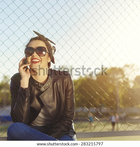 Beautiful woman in white skirt and sun glasses and leather jacket sitting near the sport place. Sun flares around
