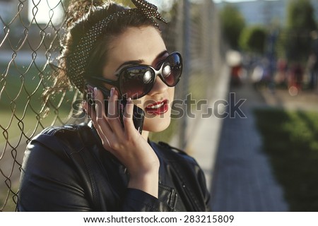 Beautiful woman in white skirt and sun glasses and leather jacket sitting near the sport place. Sun flares around