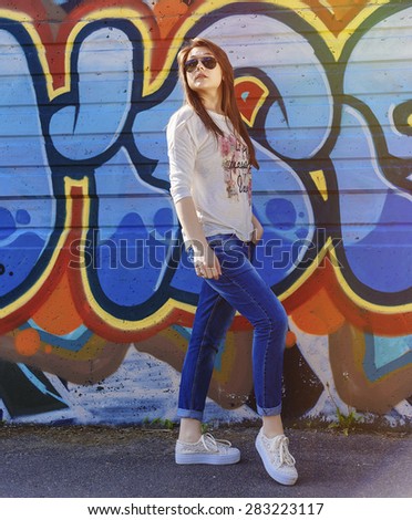 Full Length Portrait of Trendy Hipster Girl Standing at the Graffiti Brick Wall Background. Urban Fashion Concept. Copy Space.