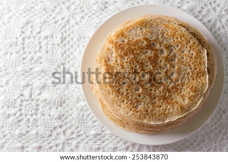 Plate with homemade yeast pancakes on a lace tablecloth. Top view