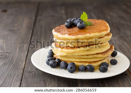 Pancakes with fresh blueberries and honey on wooden table