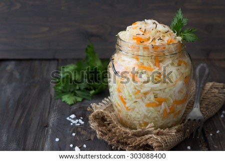 Pickled cabbage with carrots in a glass jar on a dark wooden table