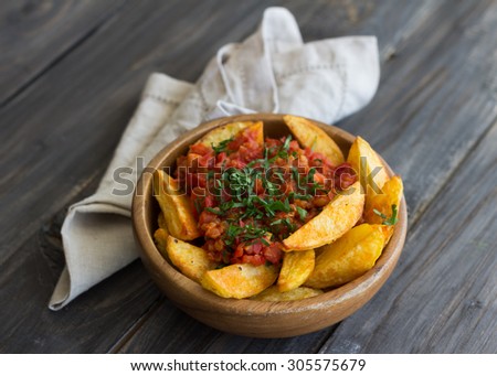 Patatas Bravas, traditional Spanish tapas, baked potatoes with spicy tomato sauce in wooden bowl on wooden table. selective focus