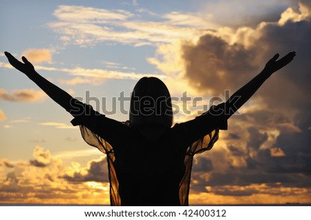 Silhouette of a young woman with outstretched hands against sunset sky