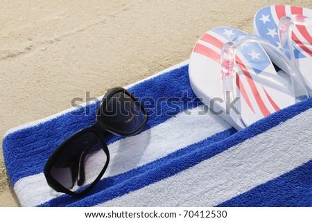 Sunglasses, flip flops and beach towel on the sand.