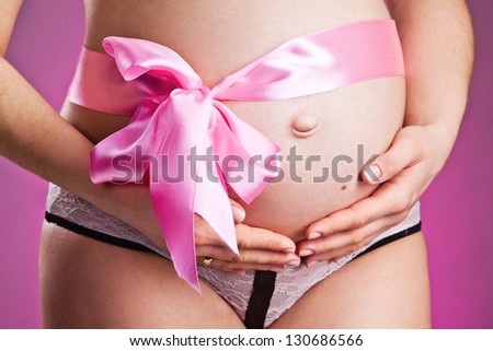 Pregnant belly with pink ribbon . Third trimester.
