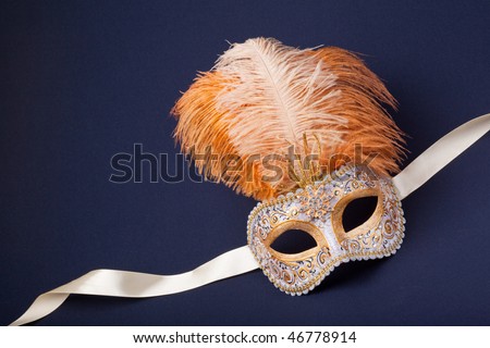 white and gold feathered mask on a dark background
