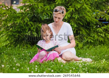 Little girl and her mother reading a book while they sitting and enjoy in beautiful nature