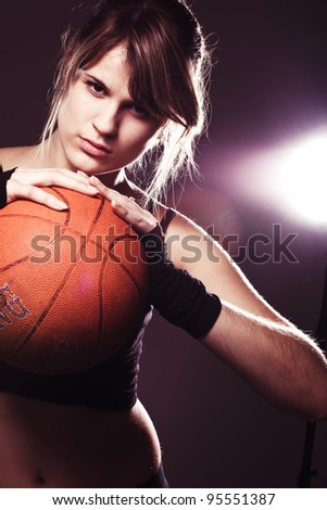 female basketball player holding ball, in black background