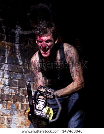 horrific madman on a dark background and gasoline-powered saw