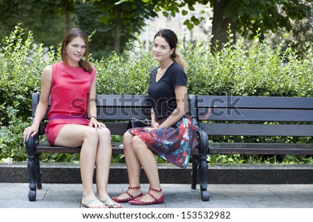 Two beautiful young woman resting on a bench in the park