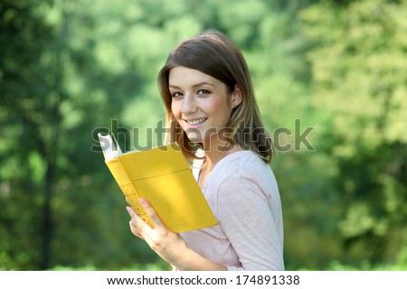 Portrait of beautiful young blonde girl reading a book in the park