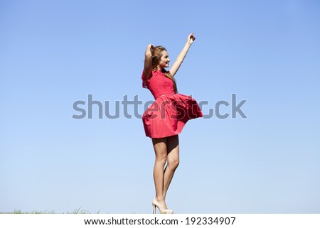 Young beautiful woman in a short red dress on a background of blue sky