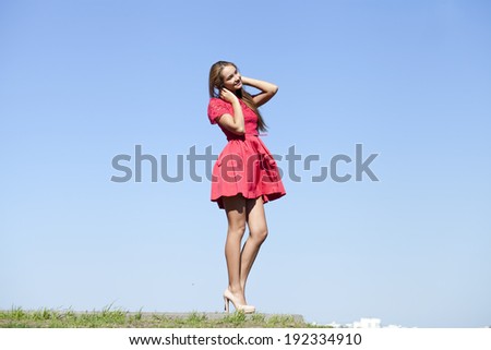 Young beautiful woman in a short red dress on a background of blue sky