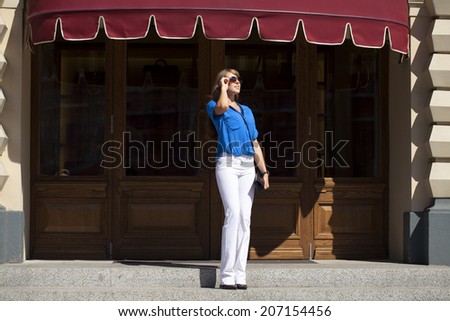 Beautiful young woman in a blue blouse and white trousers on background storefront