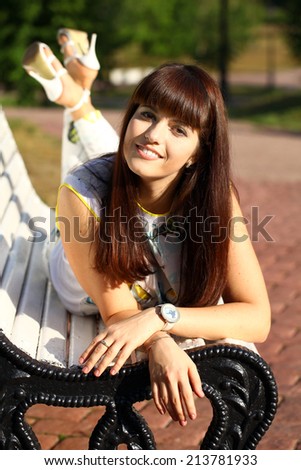 Cute young brunette woman in park sitting on the bench in summer park