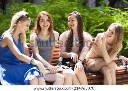 Group Of Four Teenage Girls Sitting On Bench In summer Park